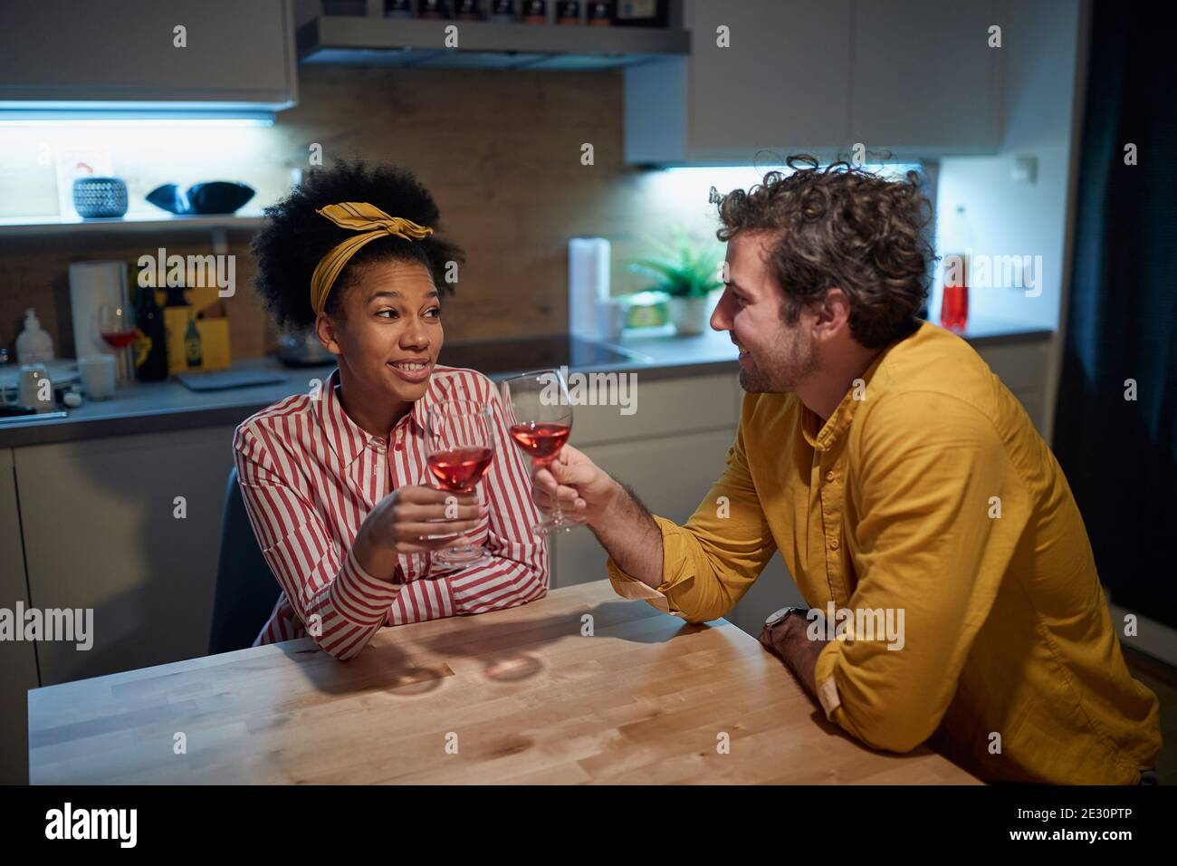 Joyful mixed couple relaxing and drinking wine together at home Stock Photo