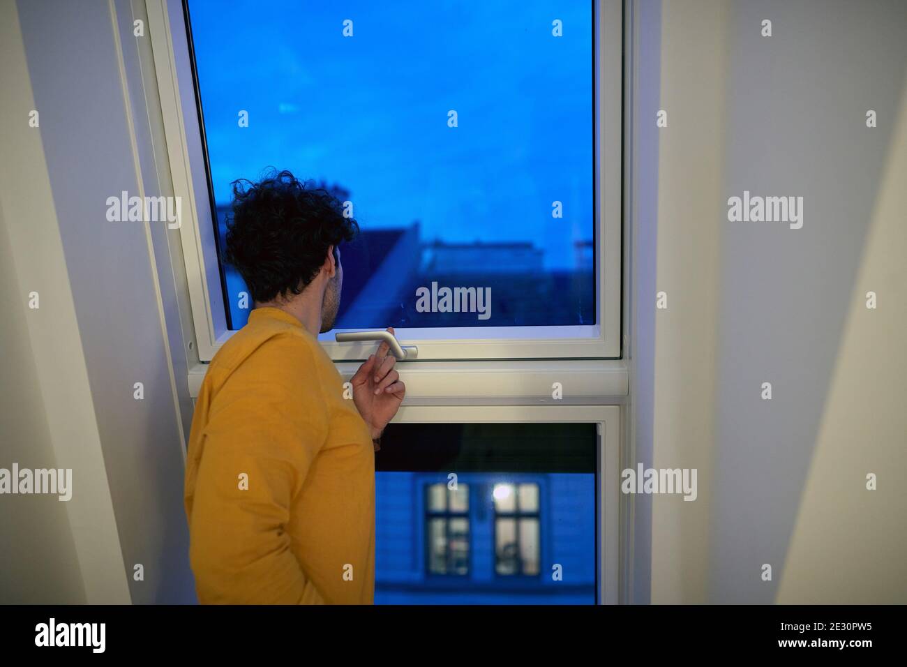 A young guy looking through the window in the home on a beautiful early morning. Morning, home, routine Stock Photo