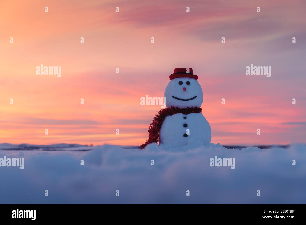 Funny snowman in stylish red hat and red scalf on snowy field during sunset. Merry Christmass and happy New Year Stock Photo