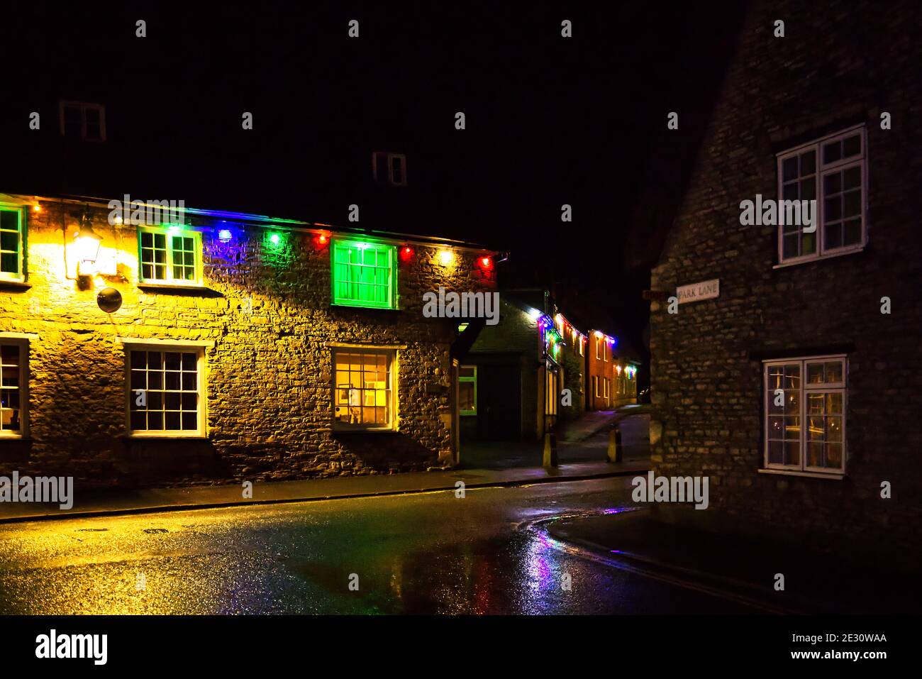 Christmas night at Sharnbrook village, Bedfordshire, UK with coloured lights decorating cottages on the High Street Stock Photo