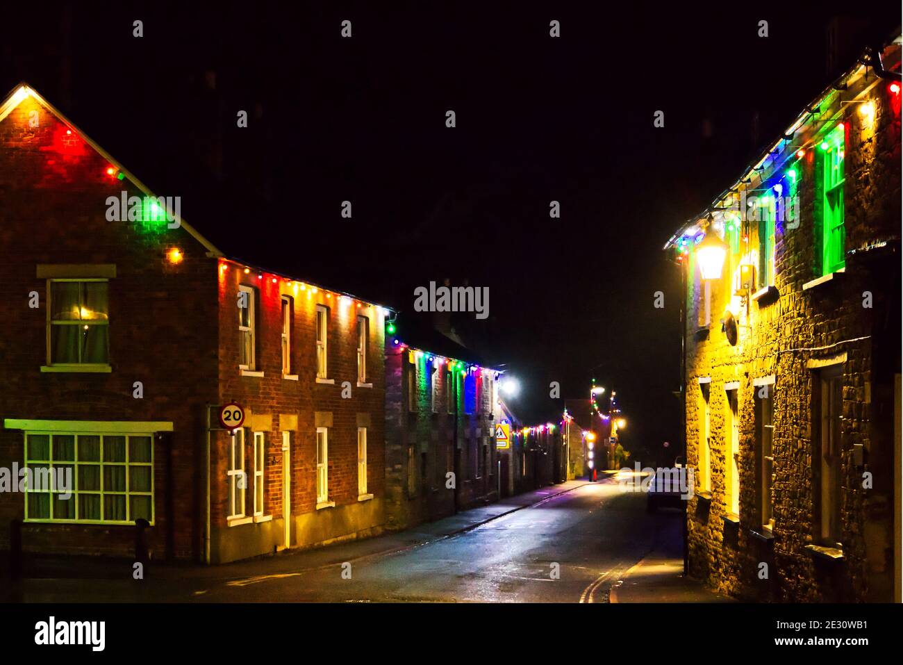 Christmas night at Sharnbrook village, Bedfordshire, UK with coloured lights decorating cottages on the High Street Stock Photo