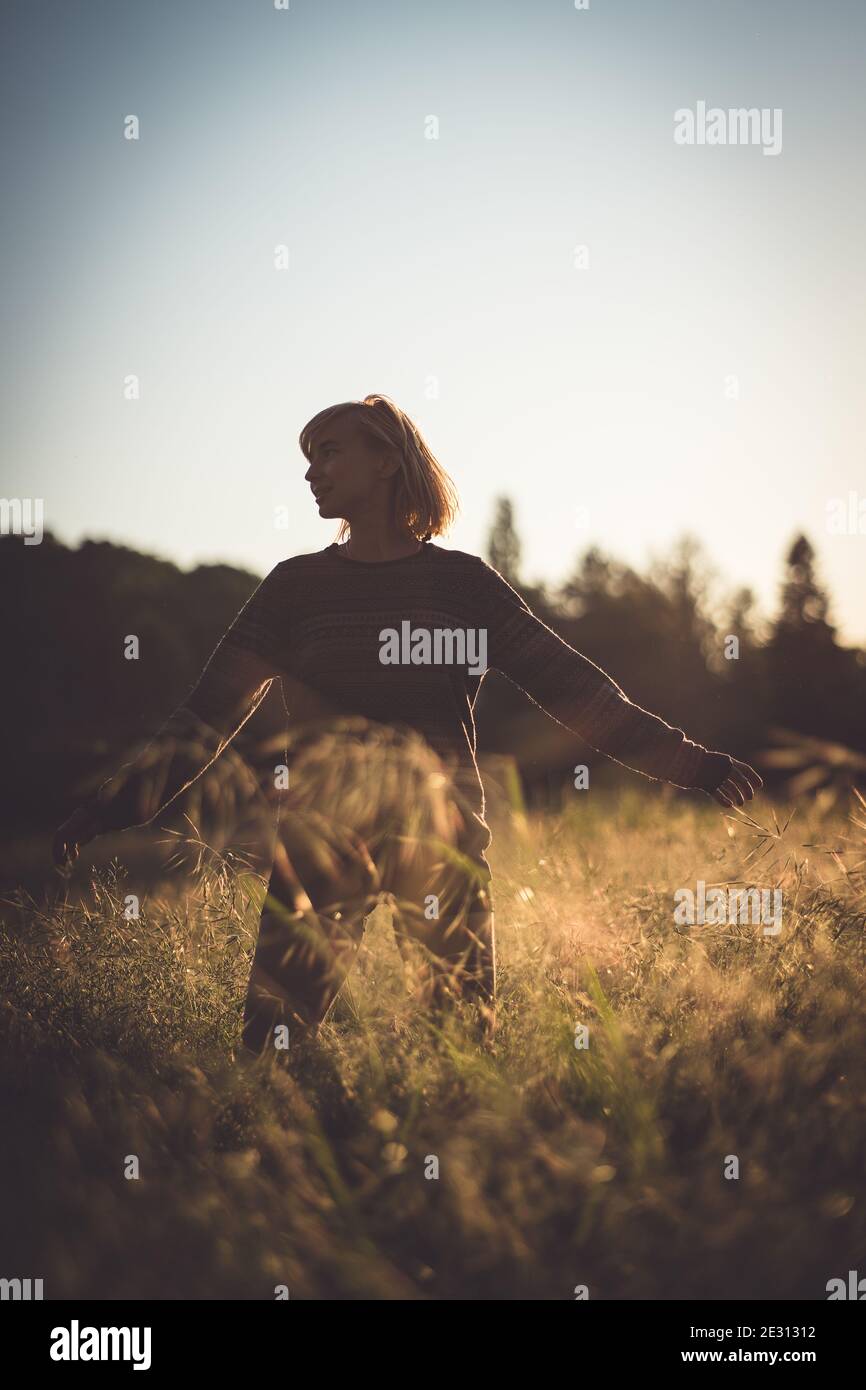 A young woman dancing in tall grass during golden hour Stock Photo