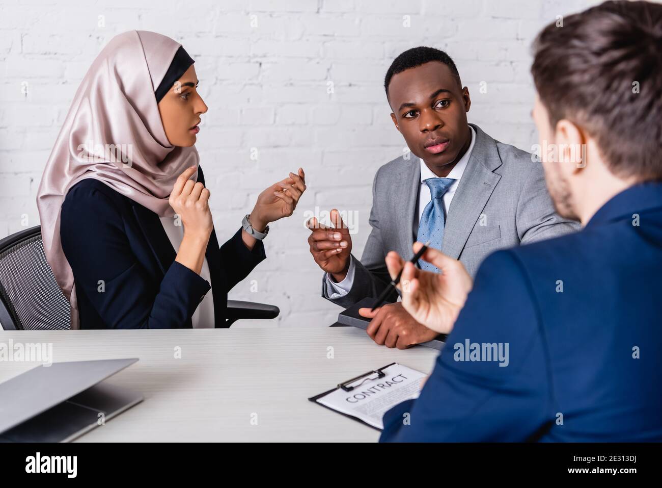 multicultural businesspeople gesturing while discussing contract near interpreter, blurred foreground Stock Photo