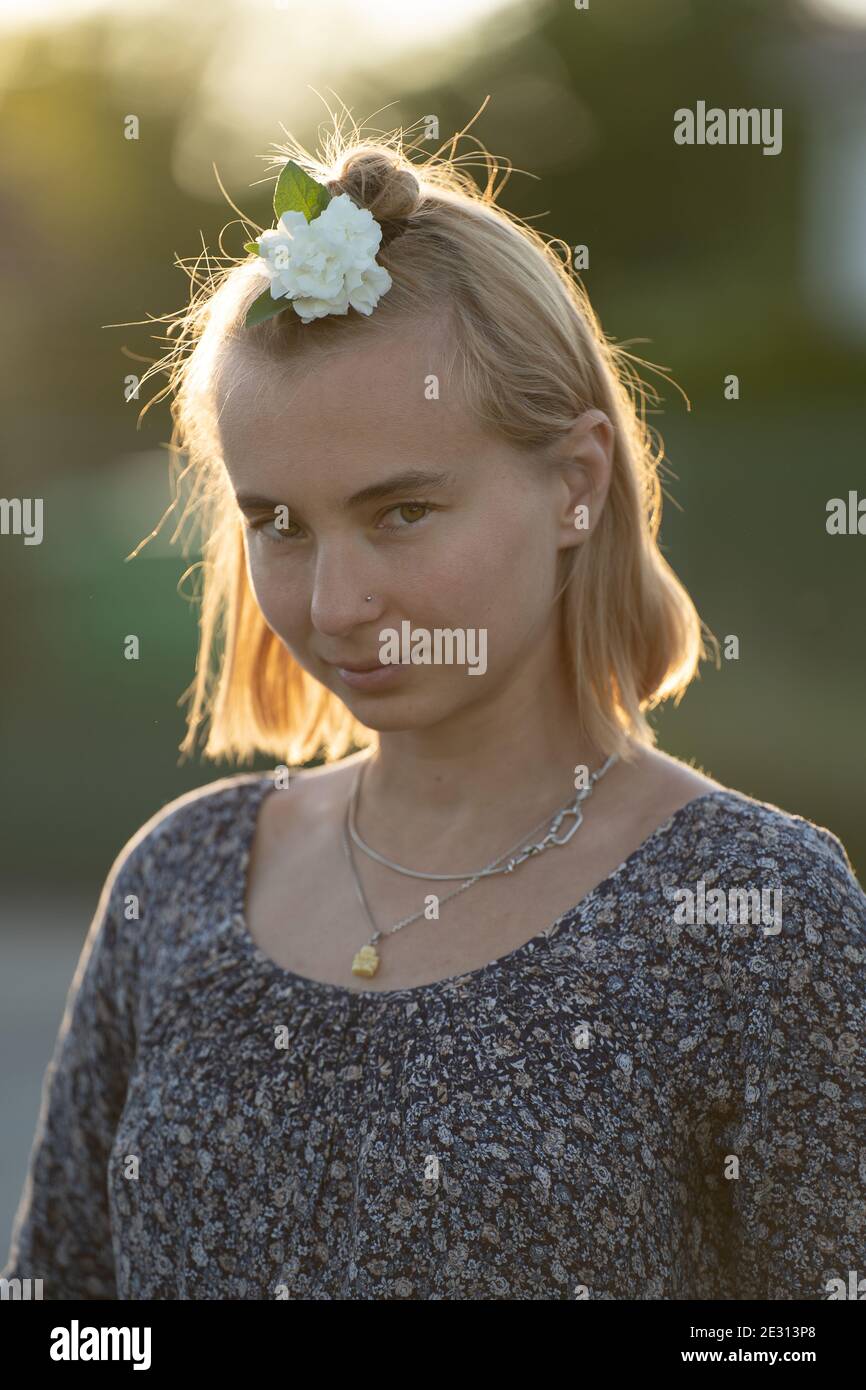 A woman with blonde hair wears a white flower in her hair, backlit by ...