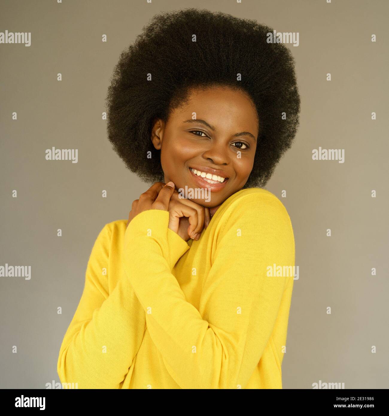 Happy Afro American millennial woman with afro hair style wear yellow sweater posing over grey wall Stock Photo