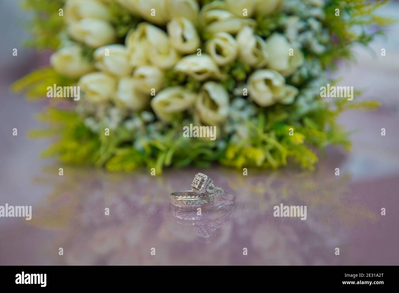 Wedding rings next to a white flower bouquet selective focuse . Bride and groom with Engagement gold rings put on the table, and next to them lies a w Stock Photo