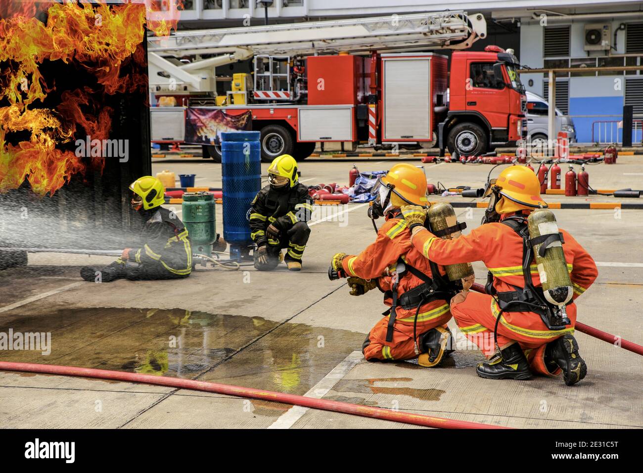 Brave firefighter using extinguisher and water from hose for fire fighting, Firefighter training with protective wear spraying high pressure water to Stock Photo