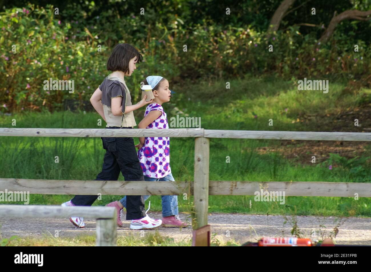 Two young girls walking along a boardwalk by a river, UK, one carrying a hot drink in a disposable cup Stock Photo