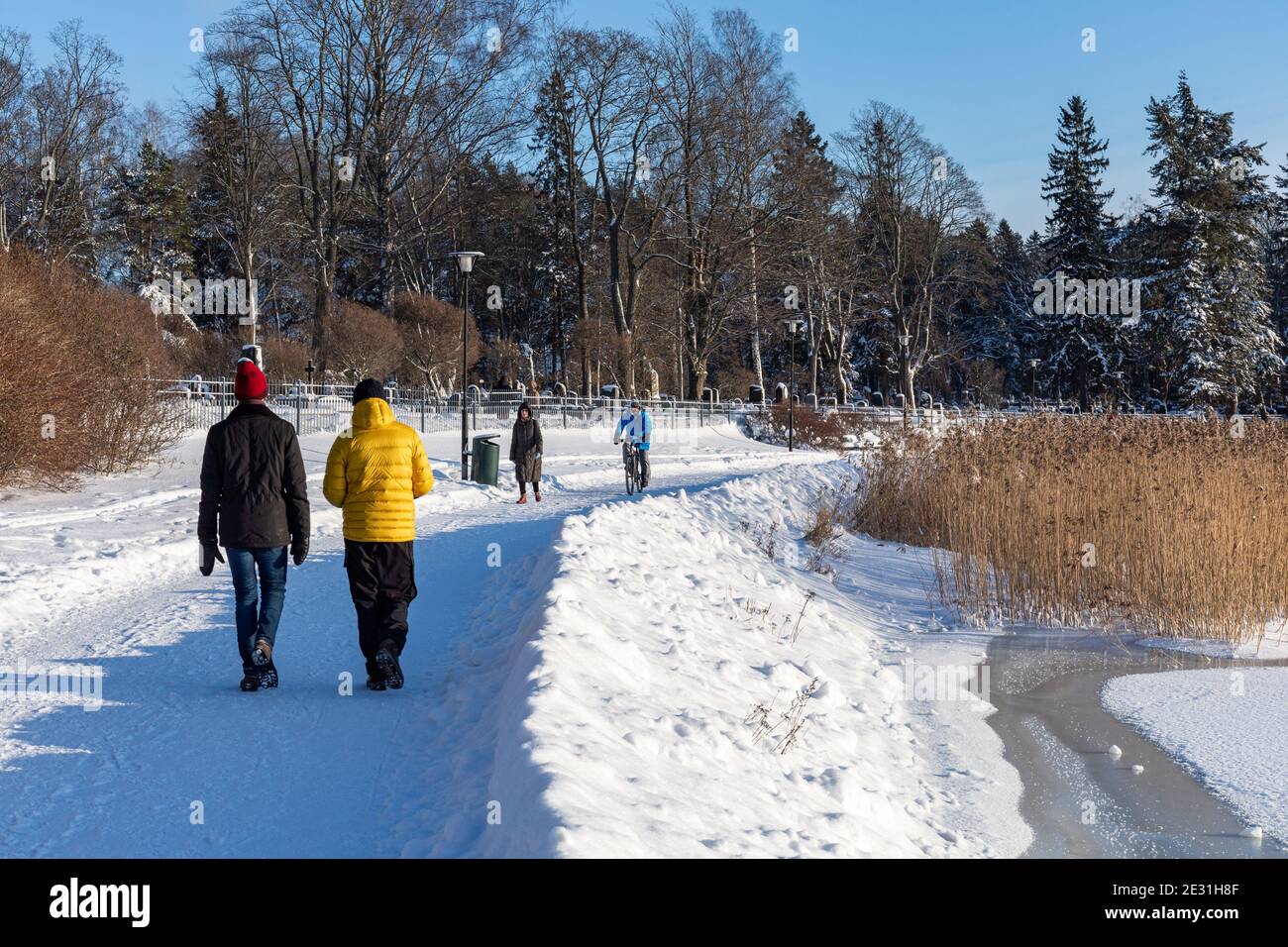 People having a Saturday stroll by frozen Lapinlahti Bay on a sunny winter day in Helsinki, Finland Stock Photo