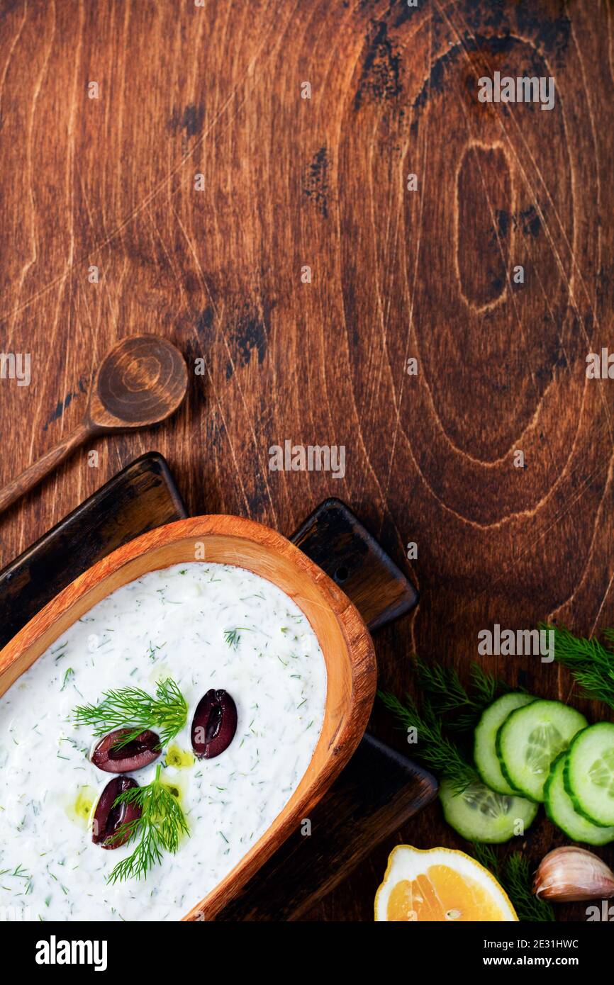 Traditional Greek sauce Tzatziki in olive wooden bowl on old rustic background. Top view. Stock Photo