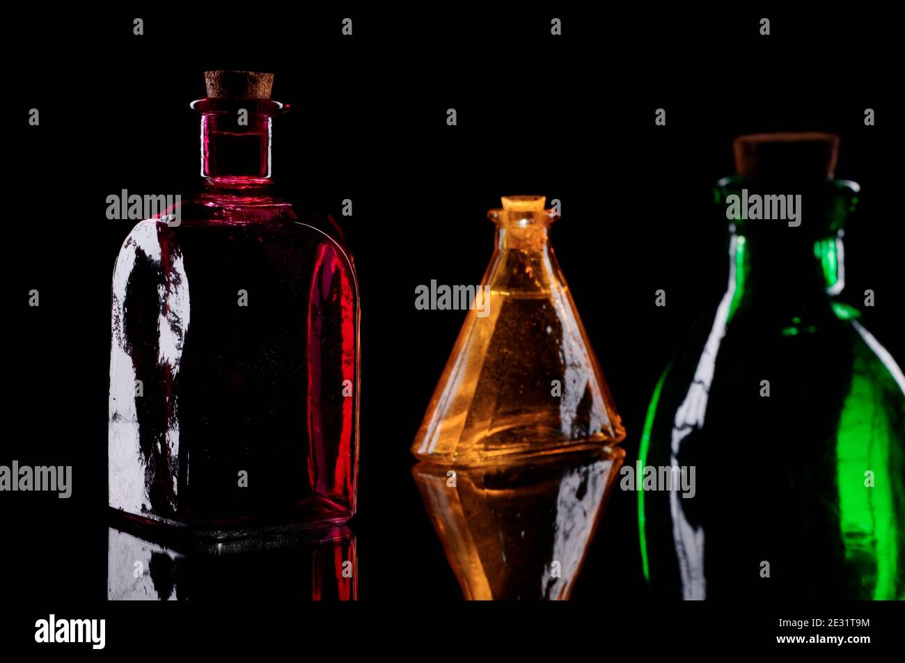Still life of three colored decorative bottles with corks on glass against black background