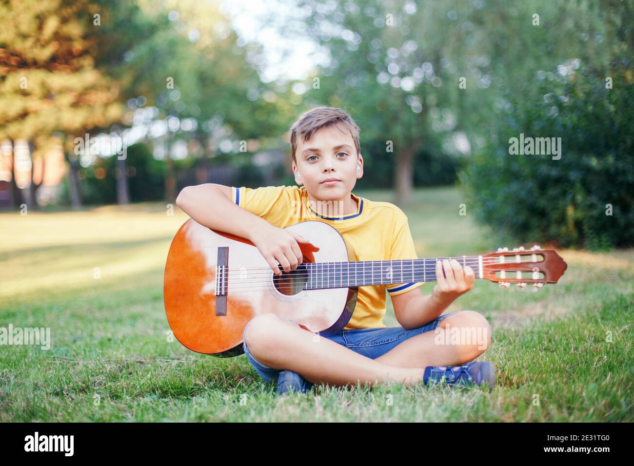 Hard of hearing preteen boy playing guitar outdoor. Child with hearing aids in ears playing music and singing song in park. Hobby art activity Stock Photo