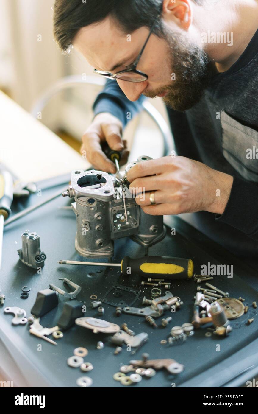 Young millennial mechanic man taking apart carburetor for restoration