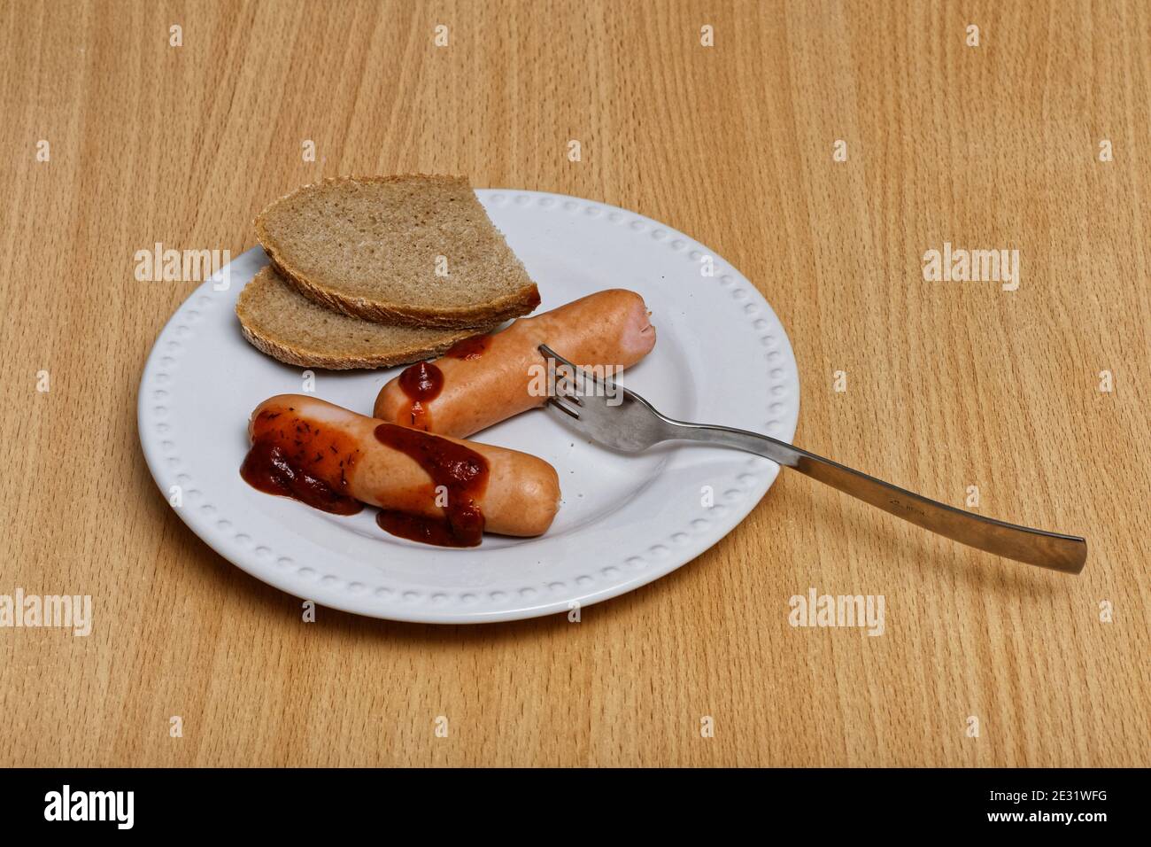 Two sausages, bread and fork on the white dish Stock Photo