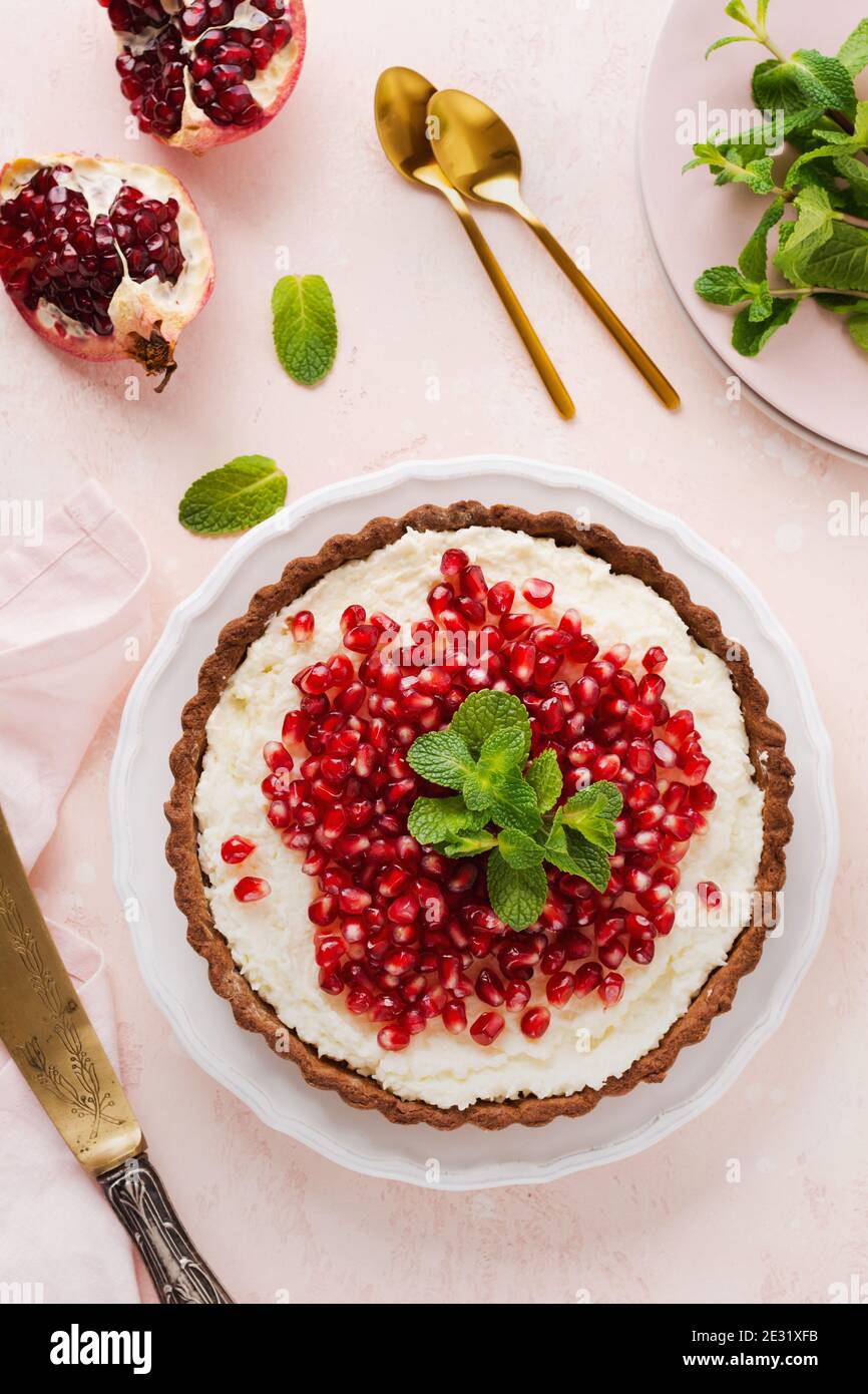 Homemade dessert chocolate tart with coconut cream and pomegranate and mint on a pink table background. Top view. Stock Photo