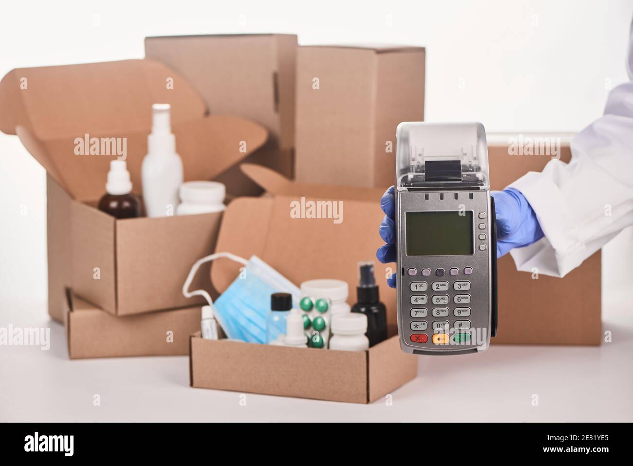 Pharmacist's hand holding a POS terminal in front of boxes with medications Stock Photo