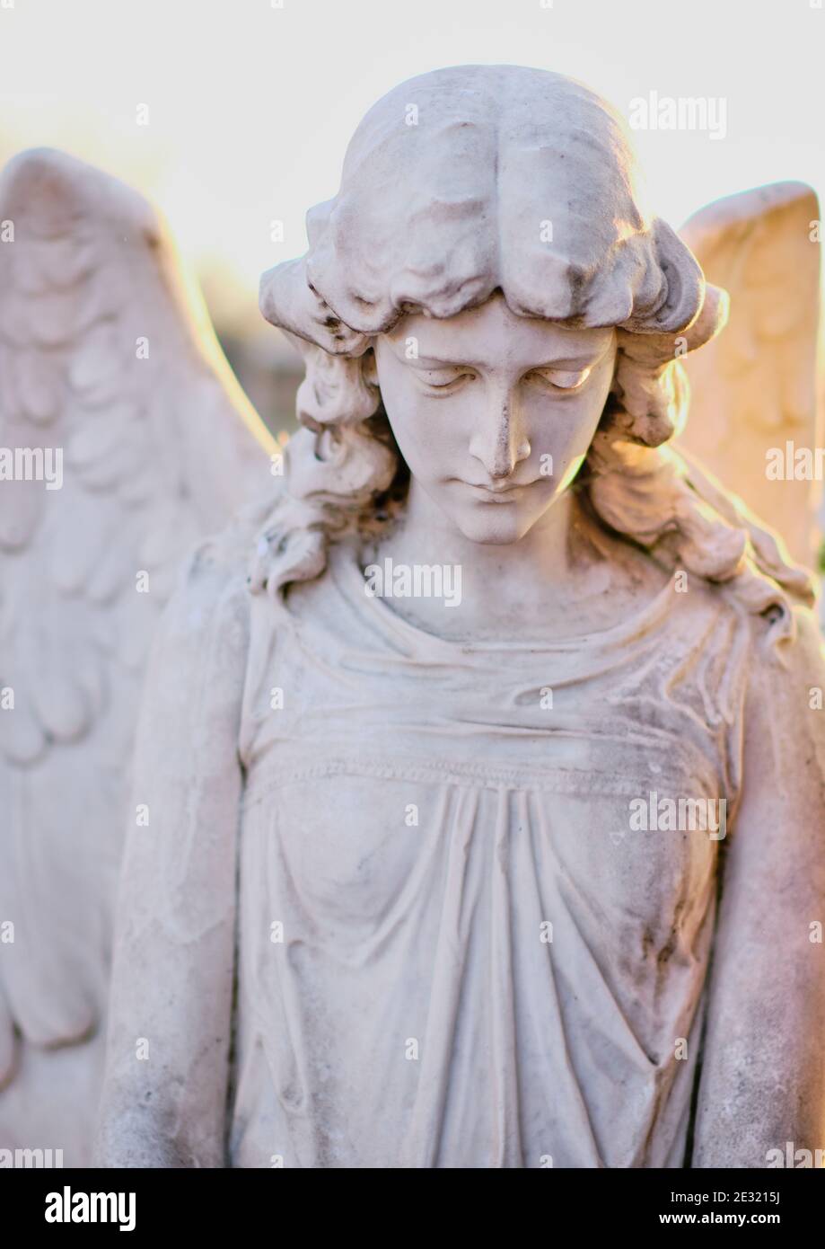 Young woman angel funeral monument with huge wings, white marble statue on a cemetery tomb. Stock Photo