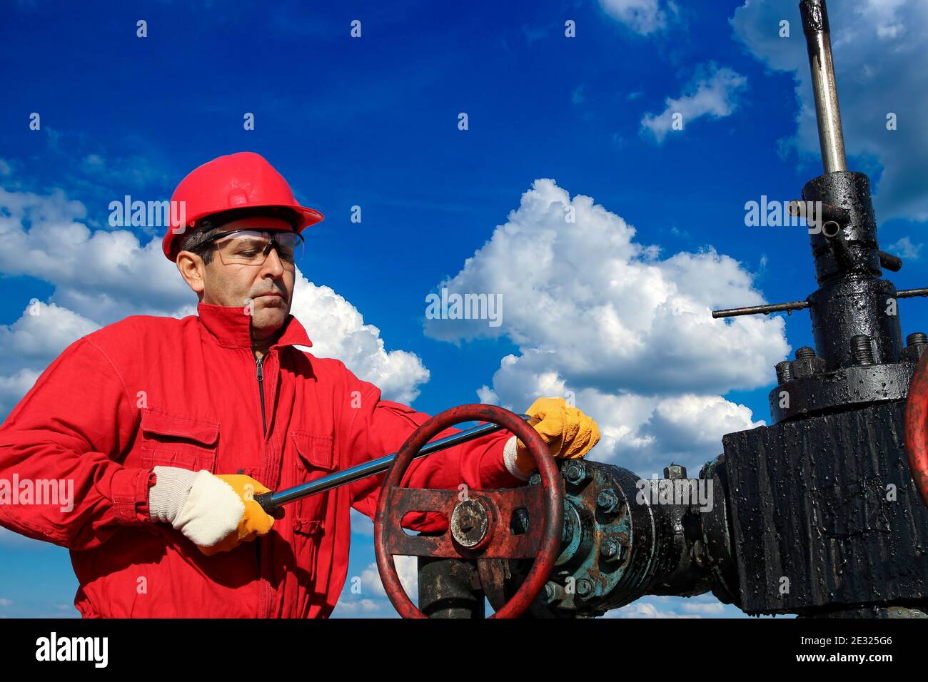 Petroleum Worker in Red Coveralls and Protective Clothing Against Blue Sky and White Clouds. Oil Rig Equipment Maintenance. Stock Photo