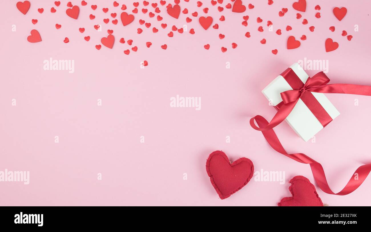 Rain of red hearts on a pink background. Gift package with ribbon bow. Coppy space. Flat lay, top wiew Stock Photo