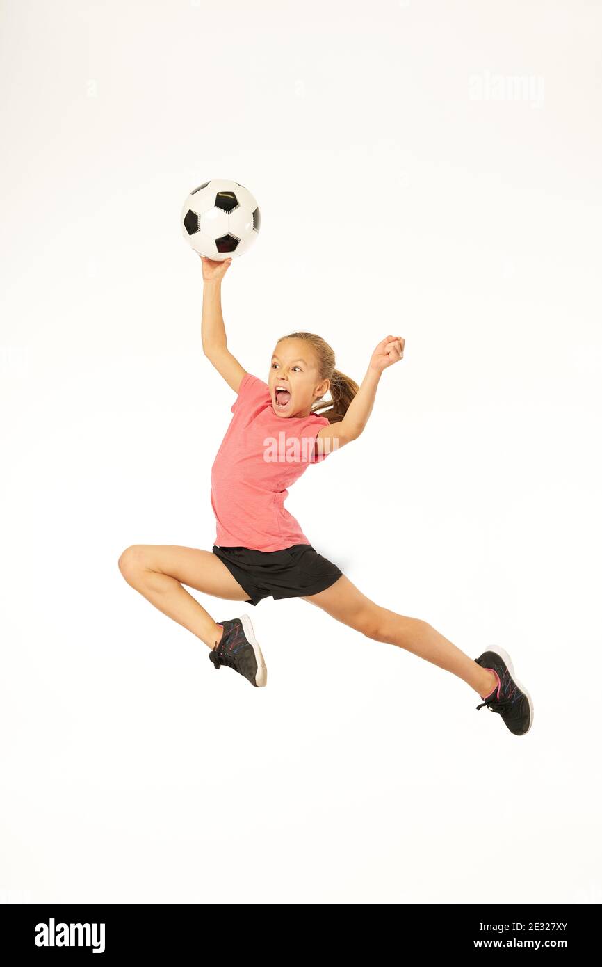 Adorable female child football player holding game ball and yelling while jumping in the air. Isolated on white background Stock Photo