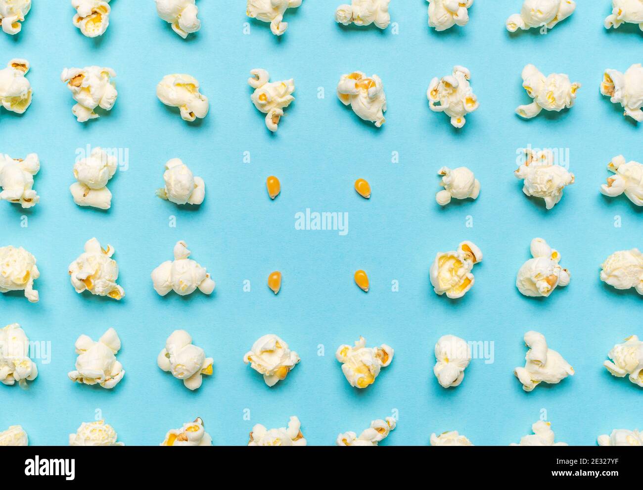 Pattern with popcorn flakes and unpopped corn aligned symmetrically on a seamless blue background. Pattern with popcorn and corn seeds, above view. Stock Photo
