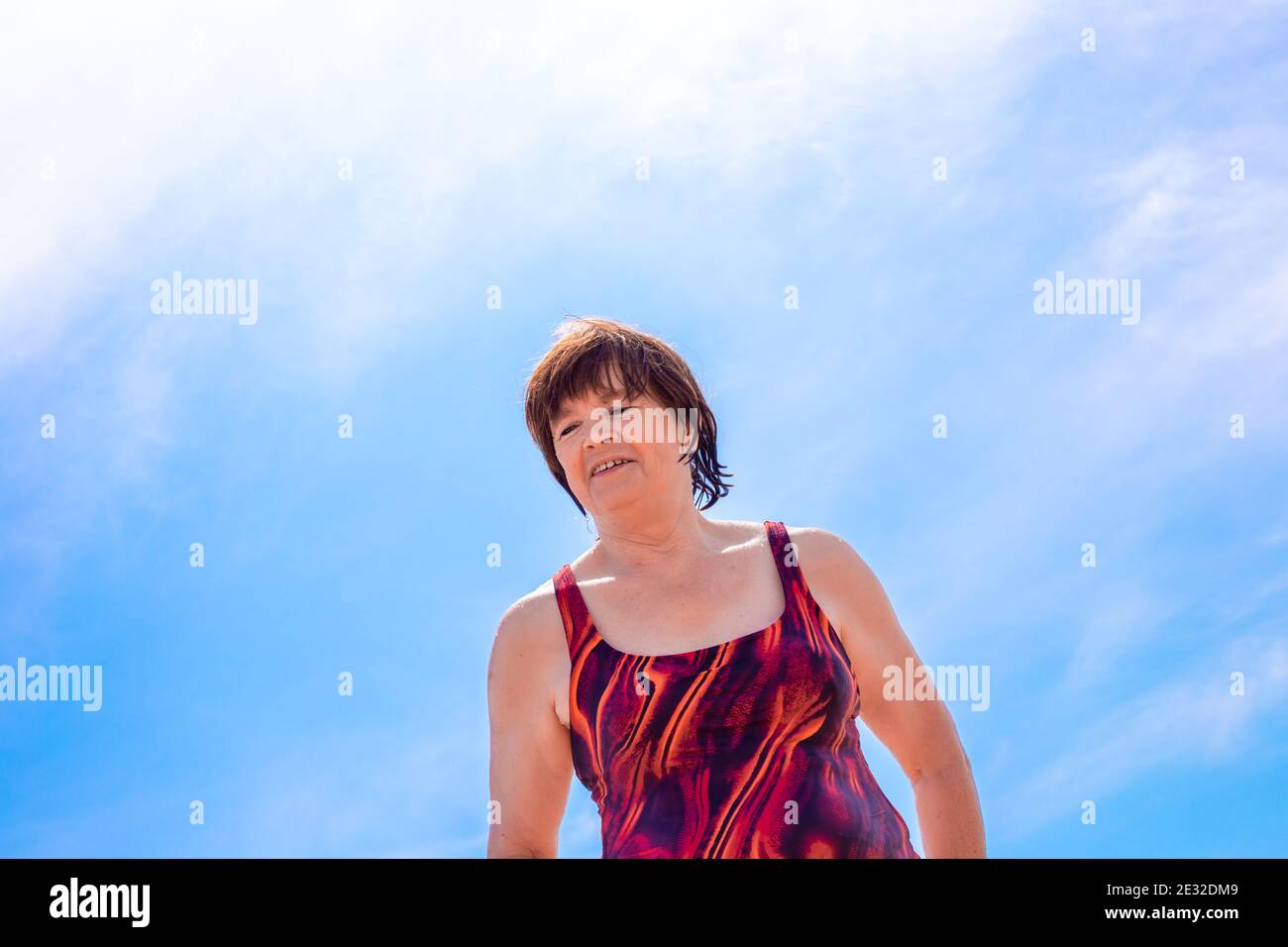 Cheerful elderly woman over 65 in a wet swimsuit against a blue sky, laughing and enjoying a summer day, quarantine ending and self-isolation Stock Photo