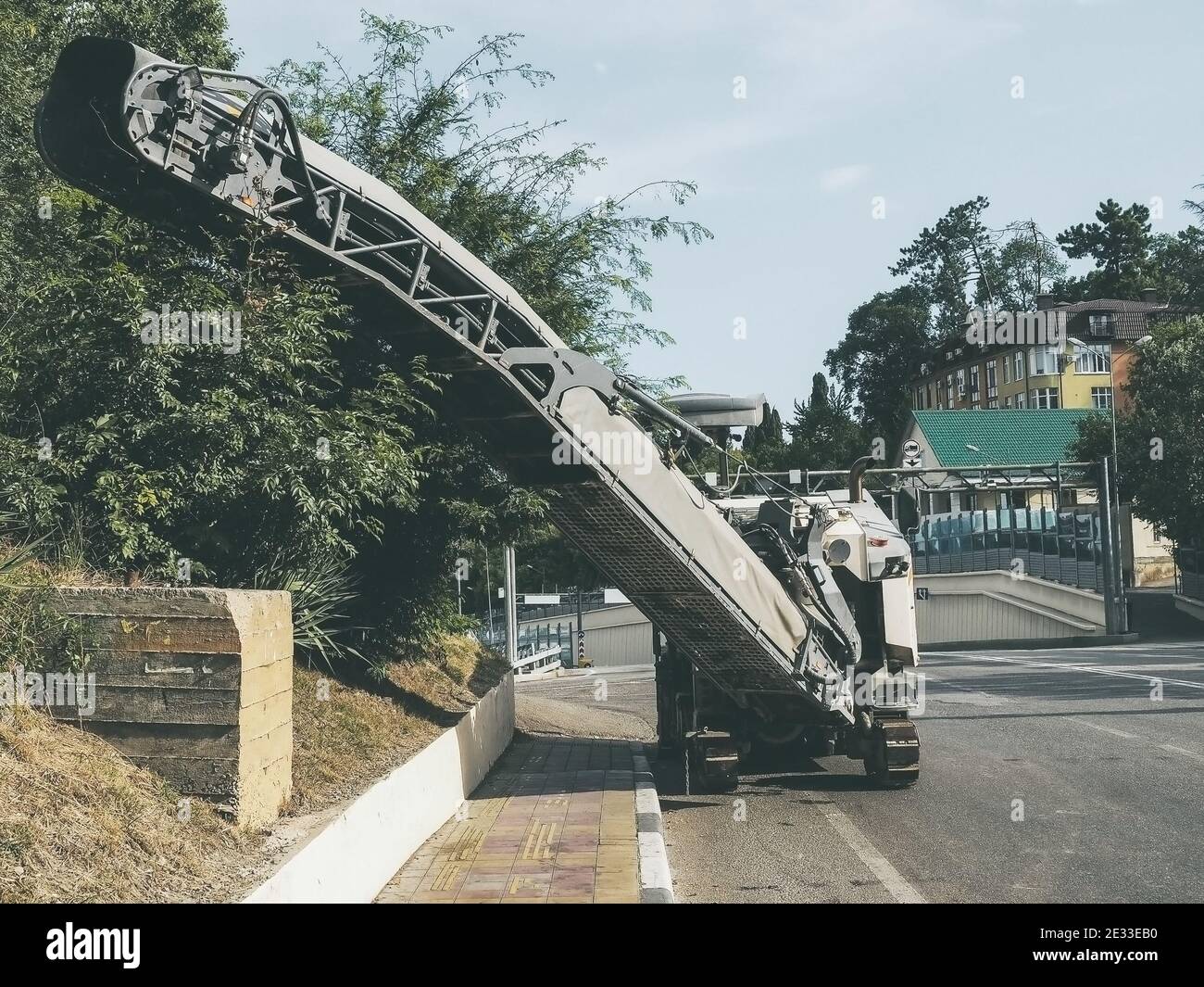 The road milling machine stands on side of the road near the sidewalk. Road service. Heavy industry Stock Photo