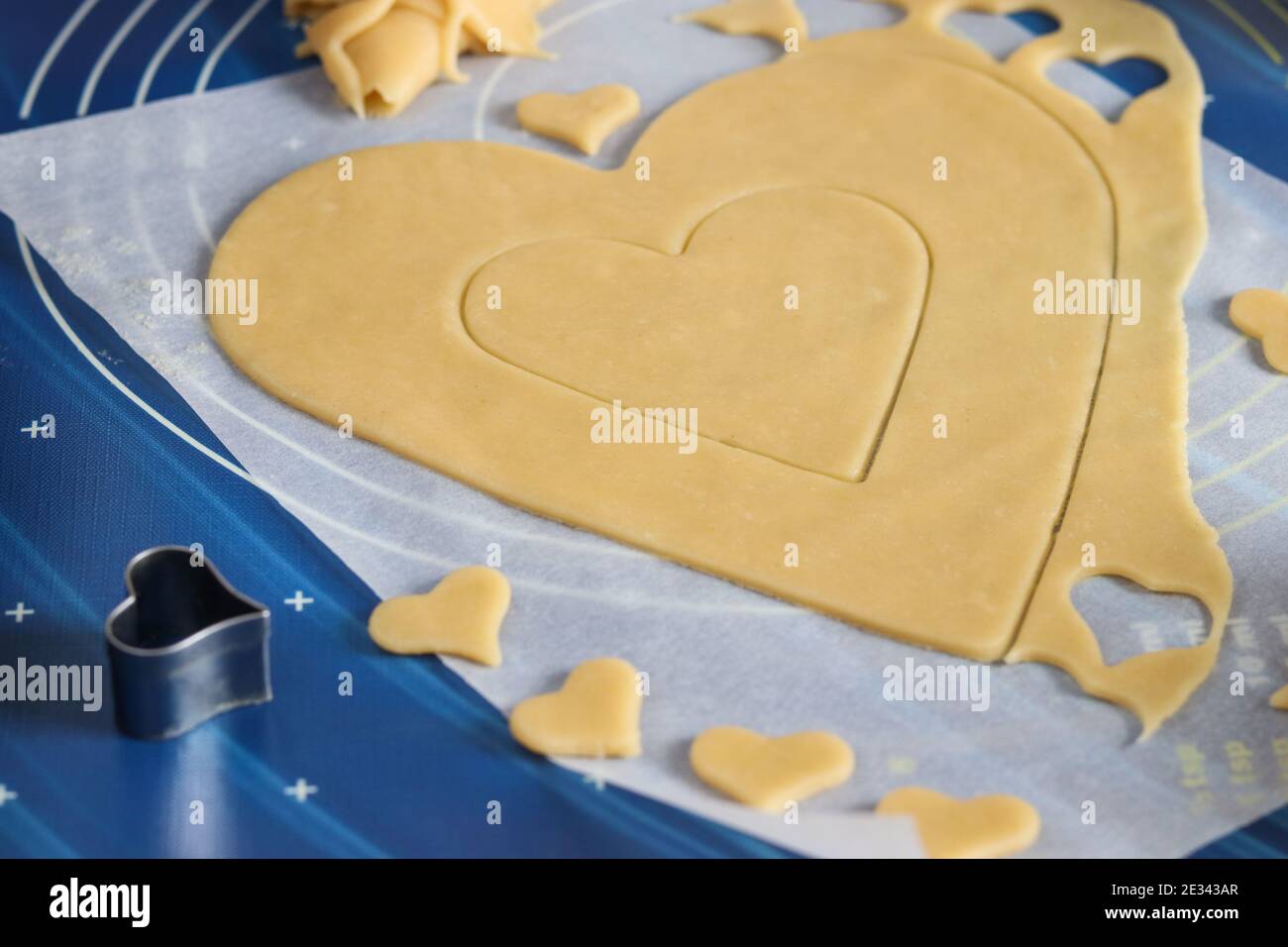 Cooking homemade heart-shaped cake. Rolling dough on the table and cutting with the help of molds. Step-by-step instruction Stock Photo