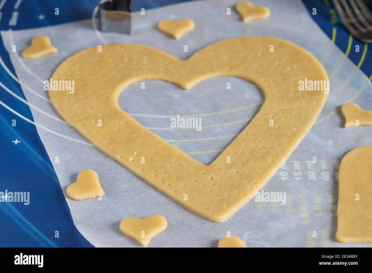 Cooking homemade heart-shaped cake. Rolling dough on the parchment and cutting with the help of molds. Step-by-step instruction Stock Photo