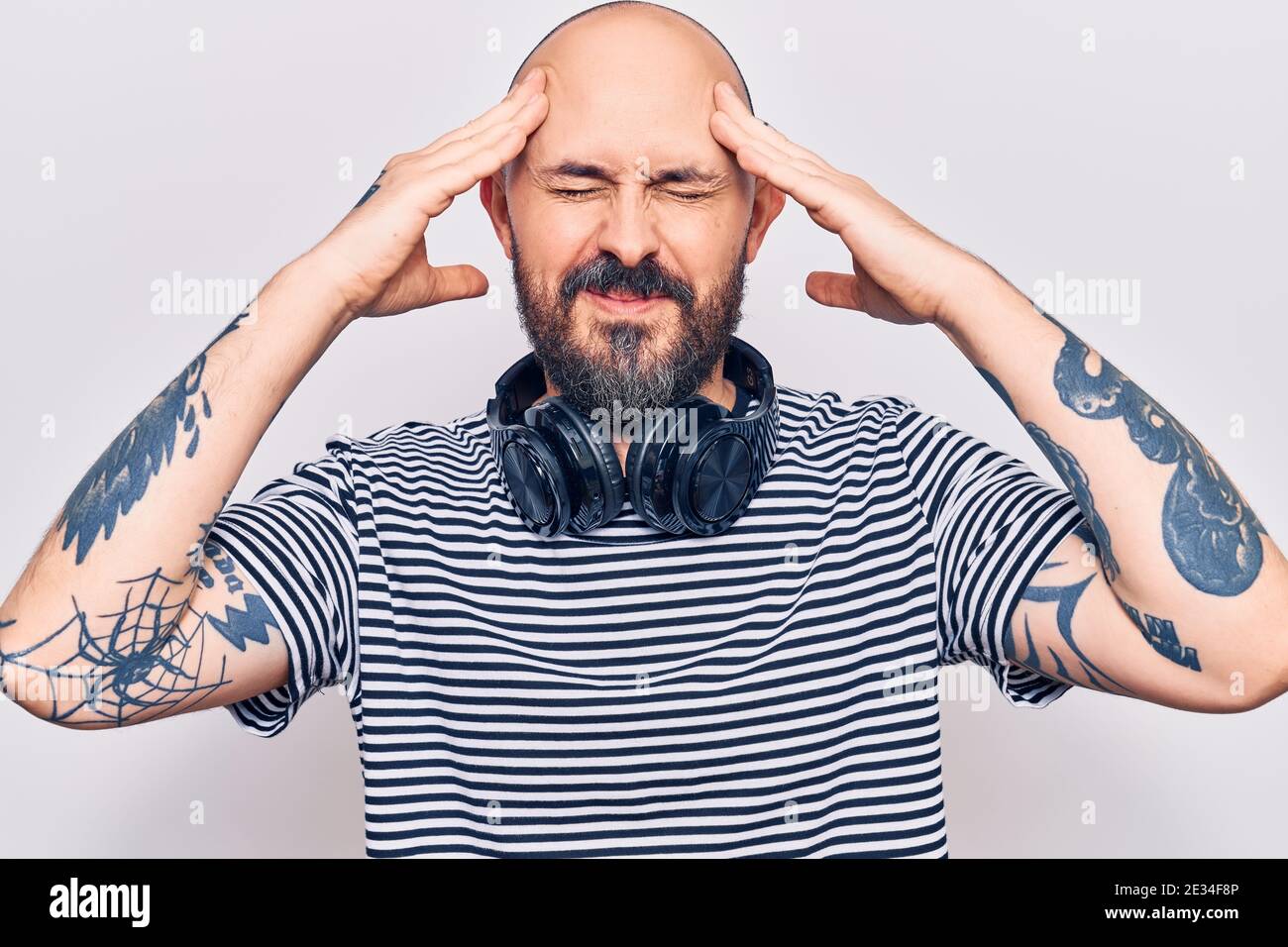 Young handsome man listening to music using headphones with hand on head, headache because