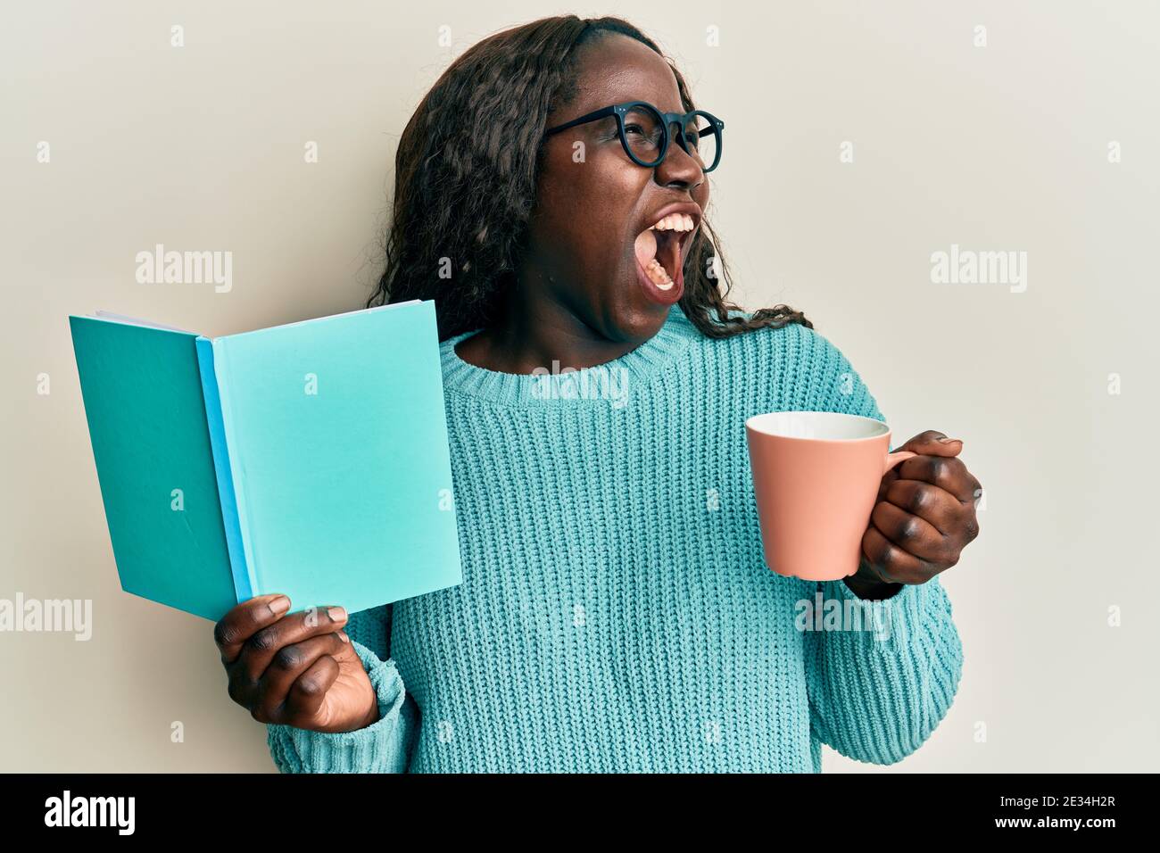 African young woman reading a book and drinking a cup of coffee angry ...