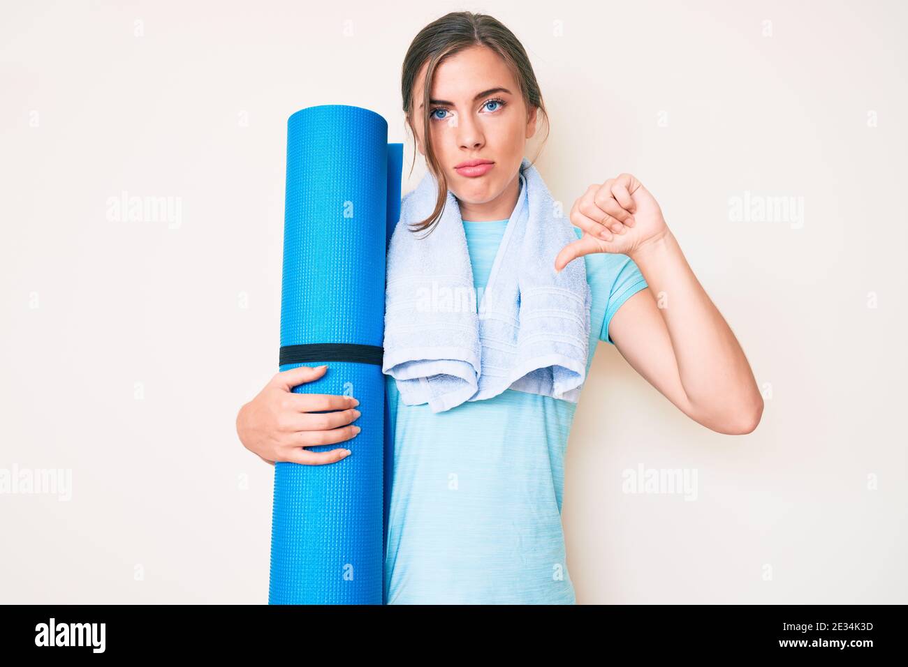 Beautiful young caucasian woman holding yoga mat with angry face ...