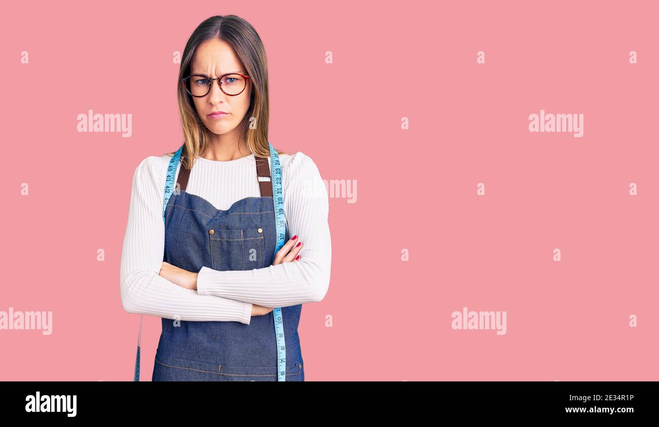 Beautiful brunette young woman dressmaker designer wearing atelier apron skeptic and nervous, disapproving expression on face with crossed arms. negat Stock Photo