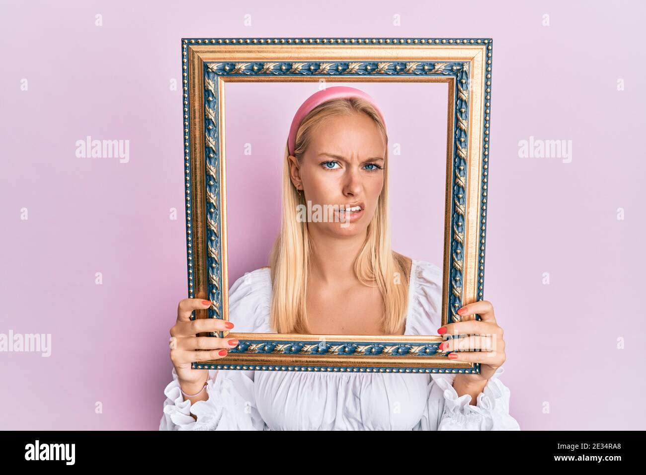 Young blonde girl holding empty frame clueless and confused expression ...