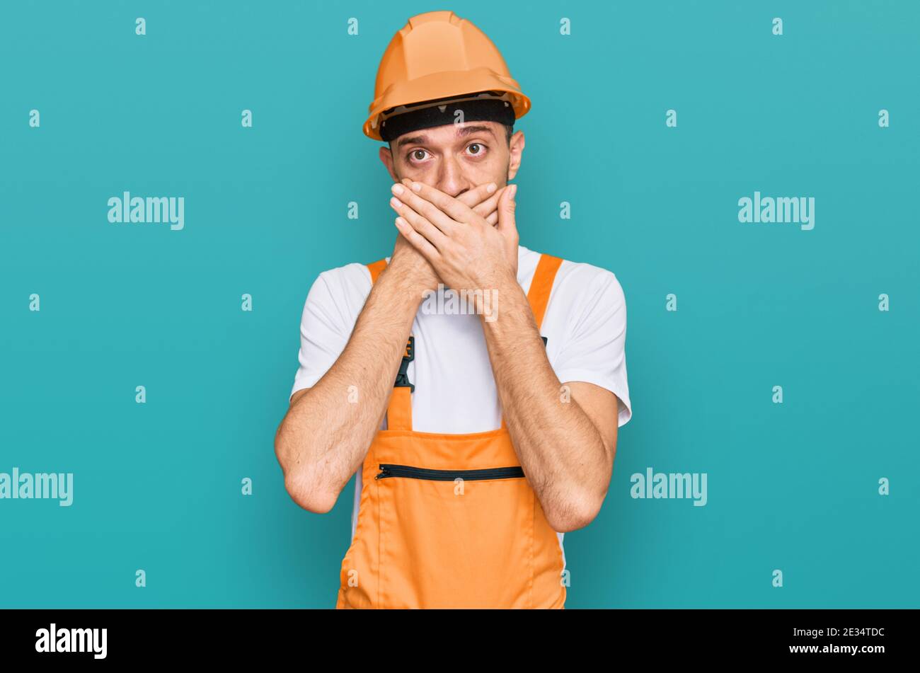 Hispanic young man wearing handyman uniform and safety hardhat shocked ...