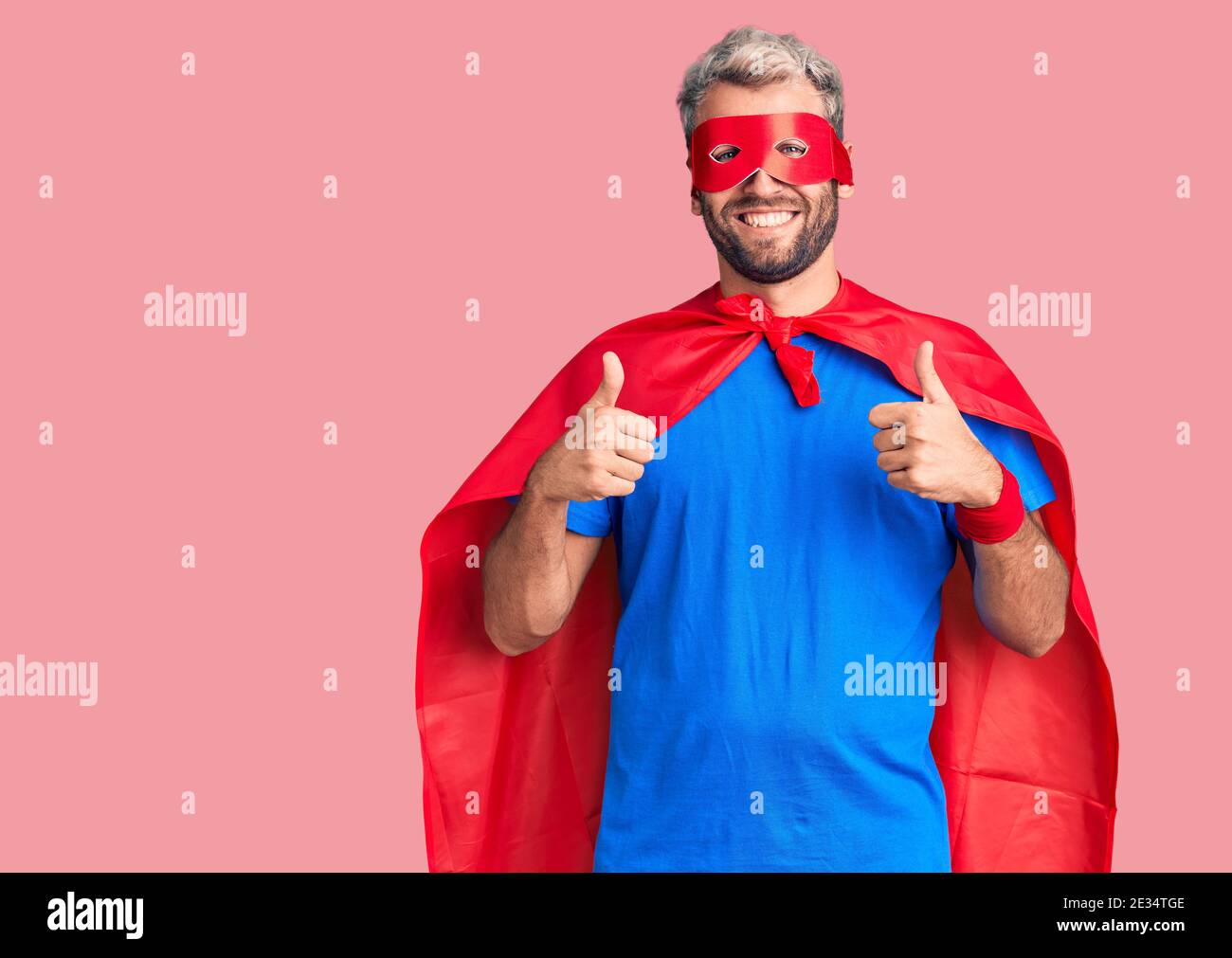 Young blond man wearing super hero custome success sign doing positive ...