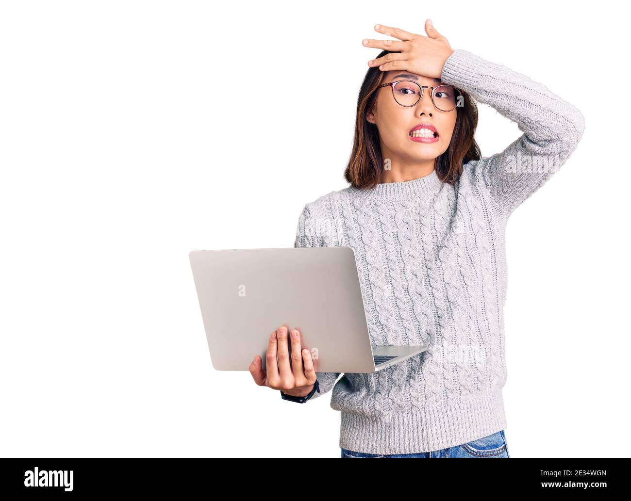 Young beautiful chinese girl wearing glasses holding laptop stressed and frustrated with hand on head, surprised and angry face Stock Photo