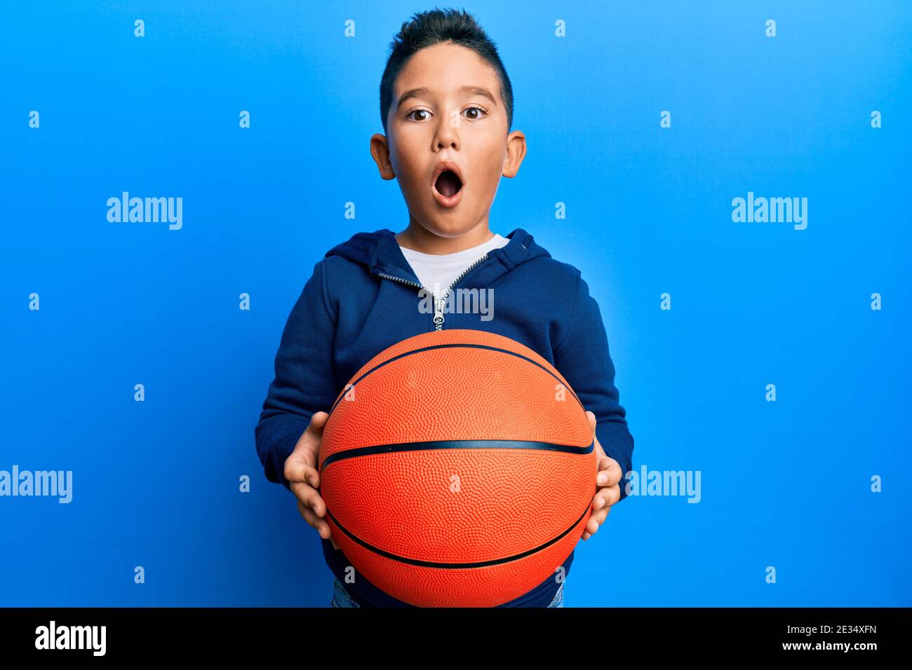 Little boy hispanic kid holding basketball ball afraid and shocked with
