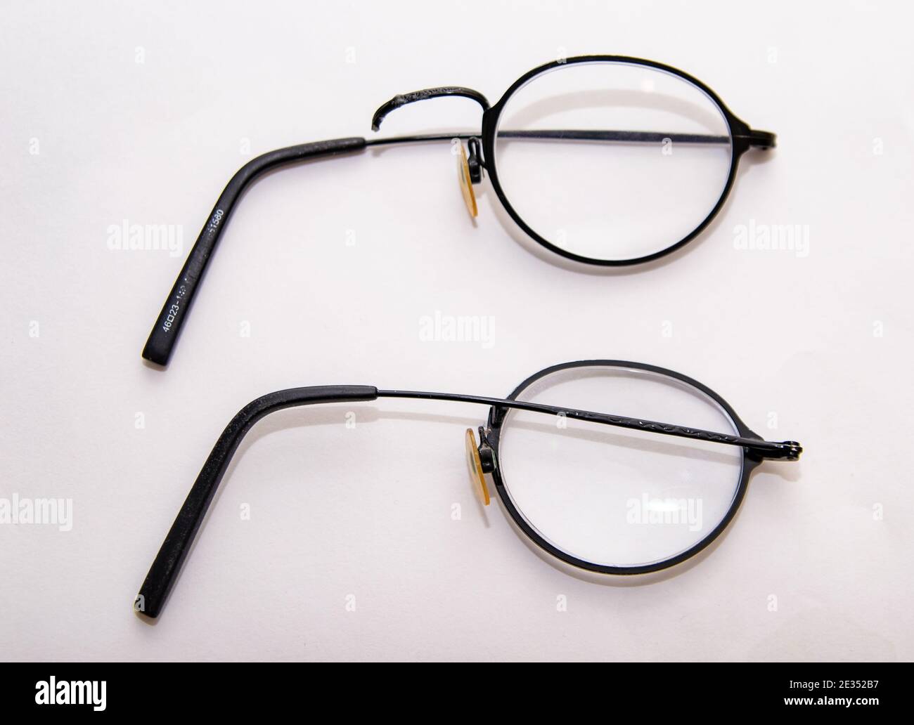 Broken glasses upon a white background. Thin round spectacles snapped at the bridge. Stock Photo