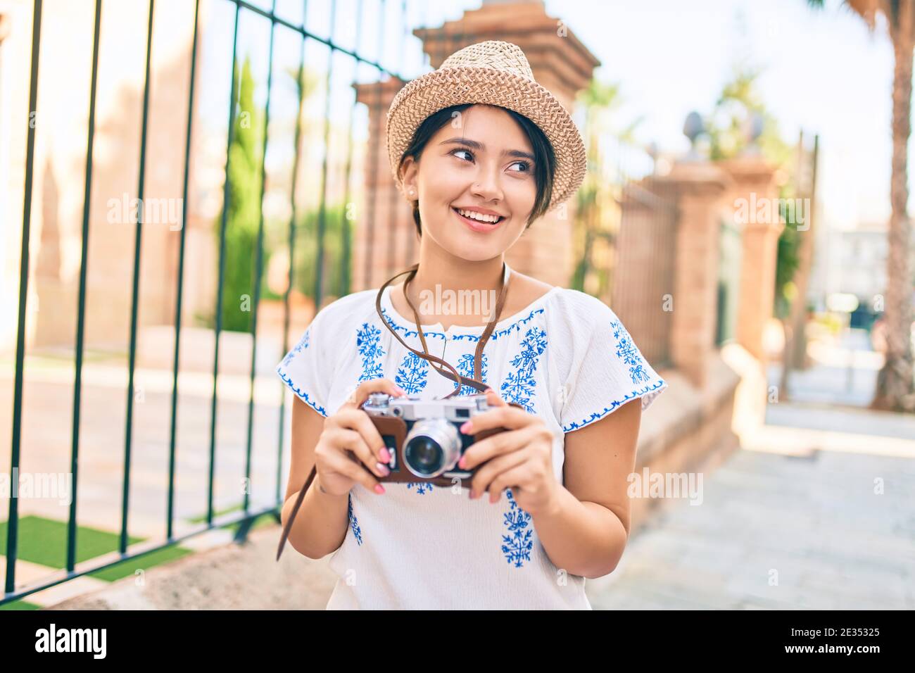 Young latin tourist girl on vacation smiling happy using vintage camera ...