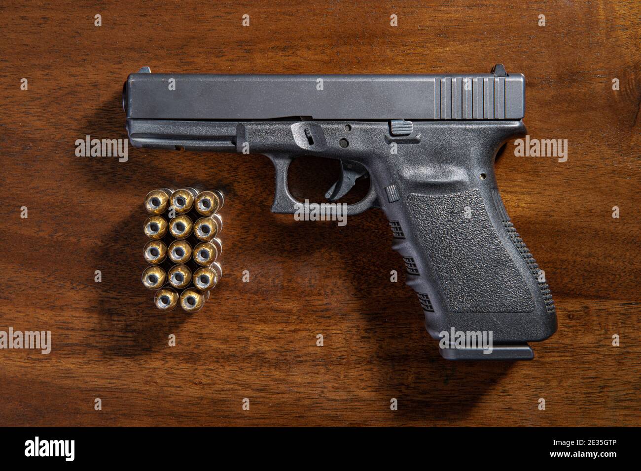A black semi-automatic pistol and ammunition on a wooden table. Stock Photo