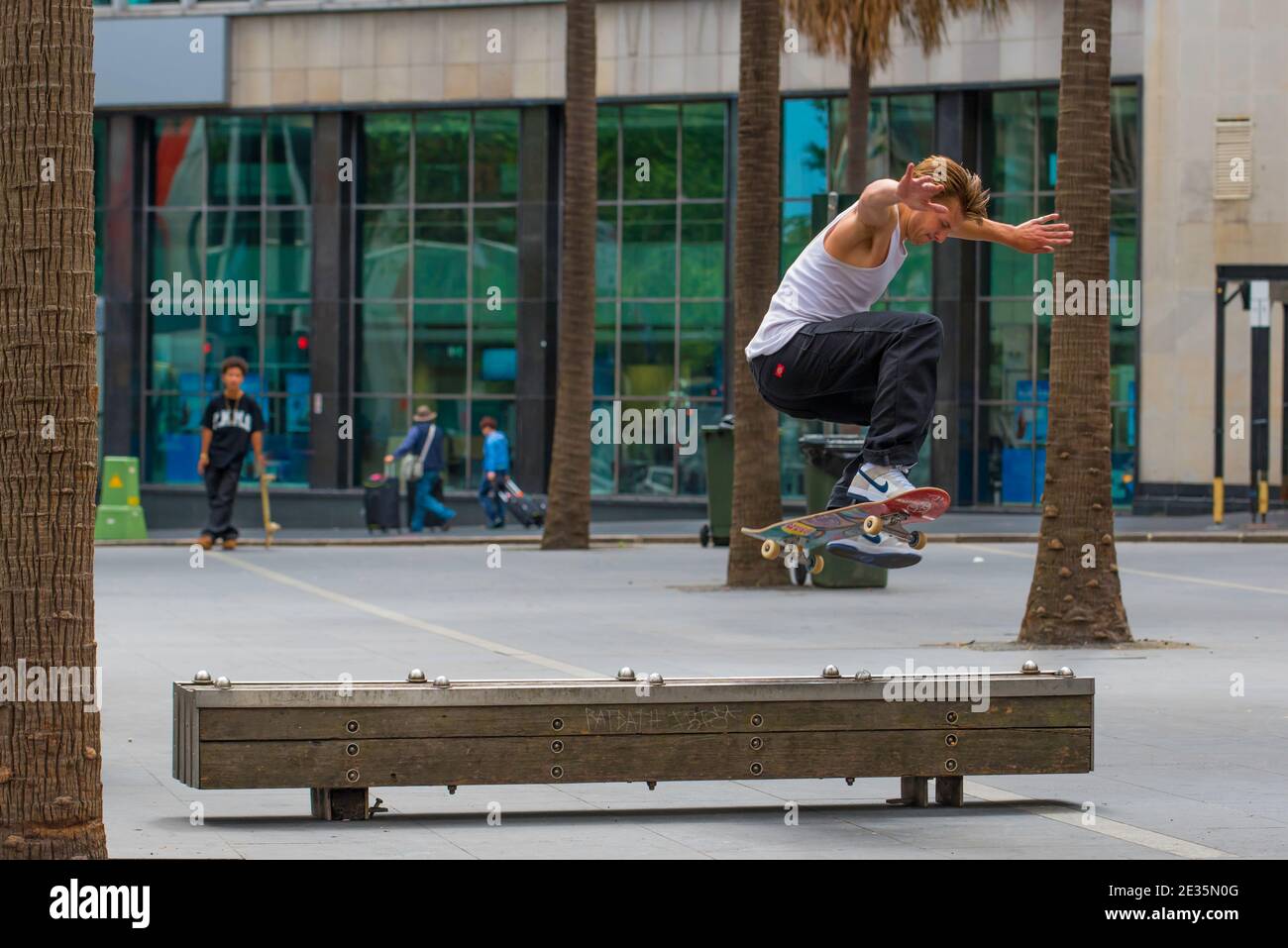 A young male Australian skateboard rider performs a flip or ollie over a timber bench in the centre of Sydney city, Australia Stock Photo