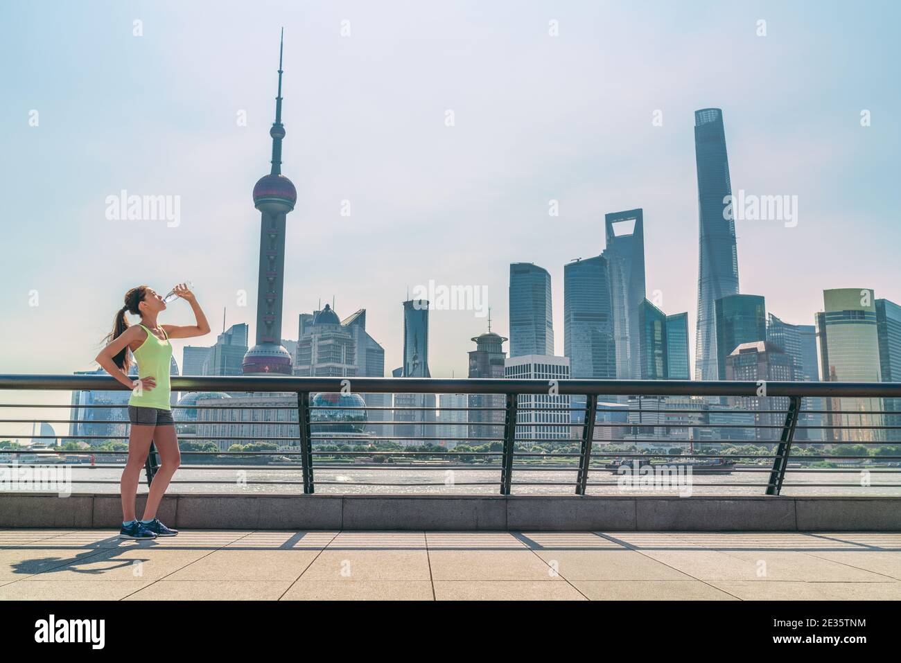 Shanghai skyline fitness woman thirsty drinking water bottle on sunny day, China. Asian jogger thirst quenching drink Stock Photo