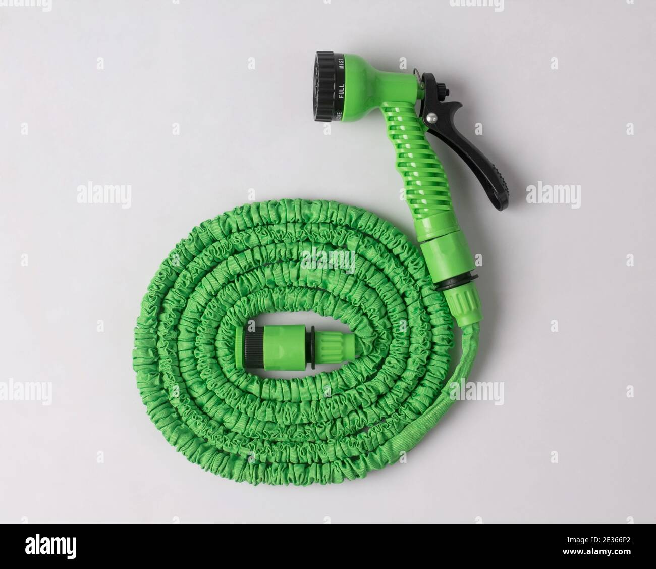 green garden hose coiled with spray nozzle isolated on white background Stock Photo