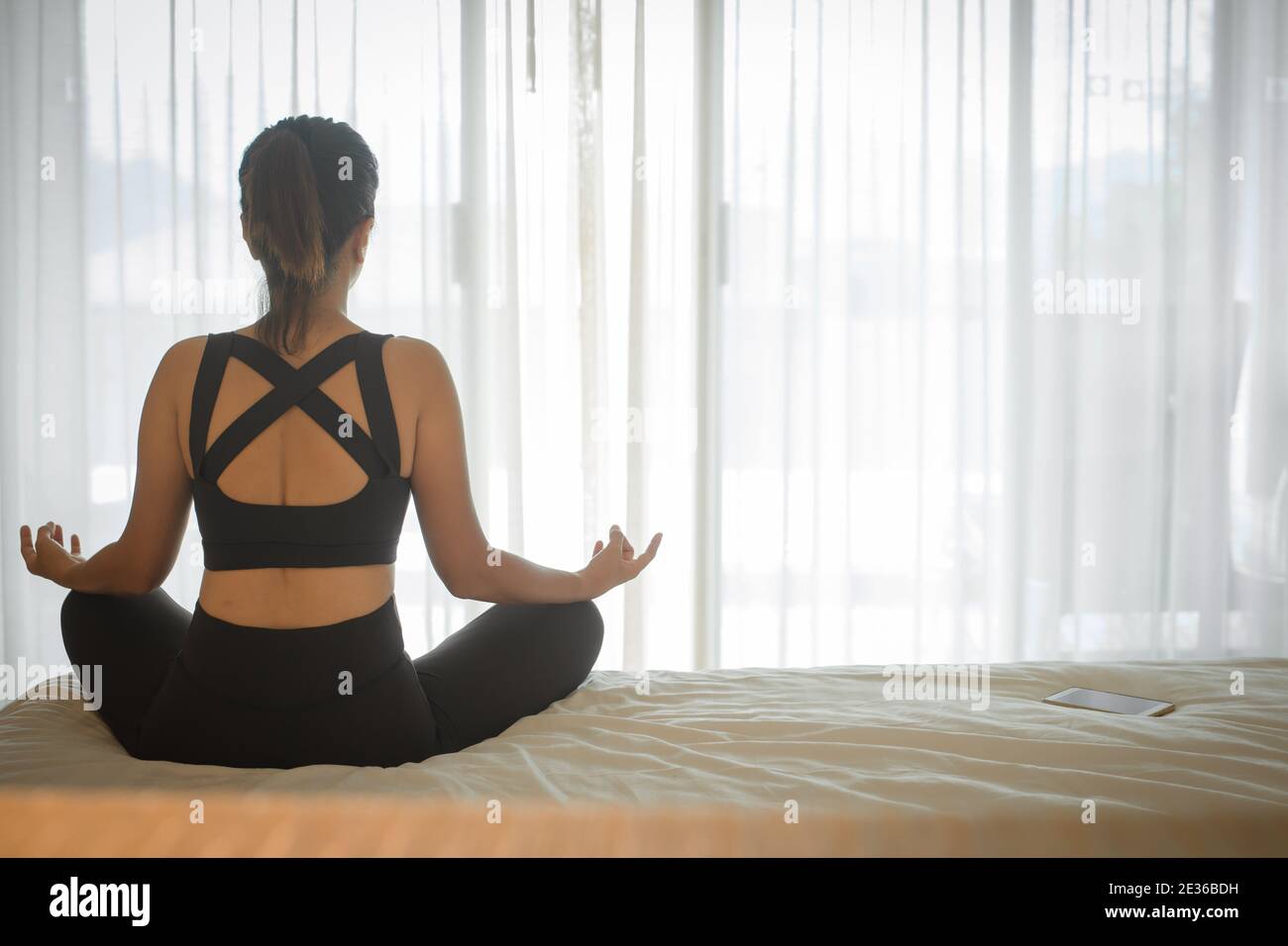 Woman doing yoga exercise on bed at home. Morning workout in bedroom. Healthy and sport lifestyle. Stock Photo