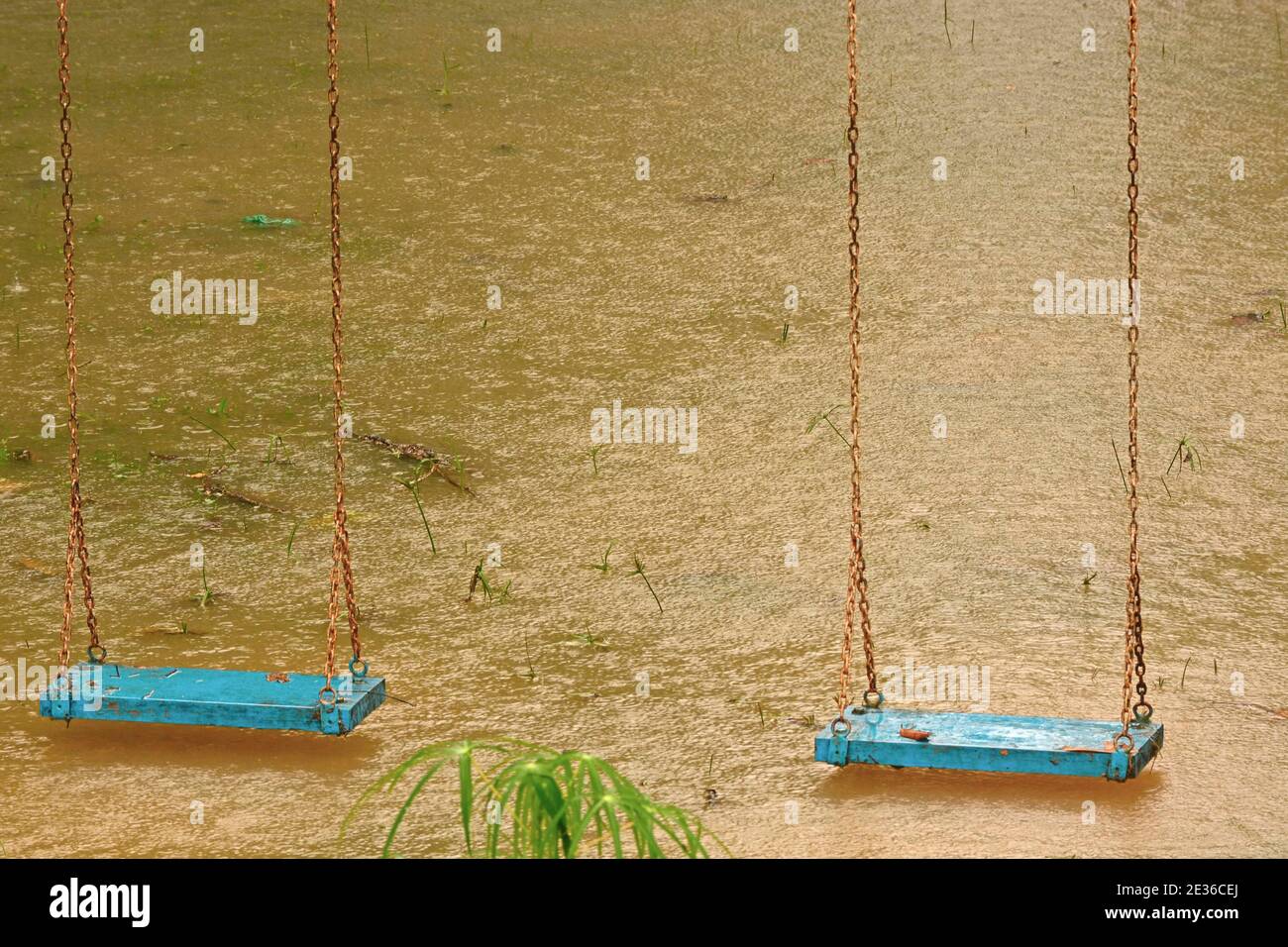 Playground swings with flooded ground and grass underneath Stock Photo
