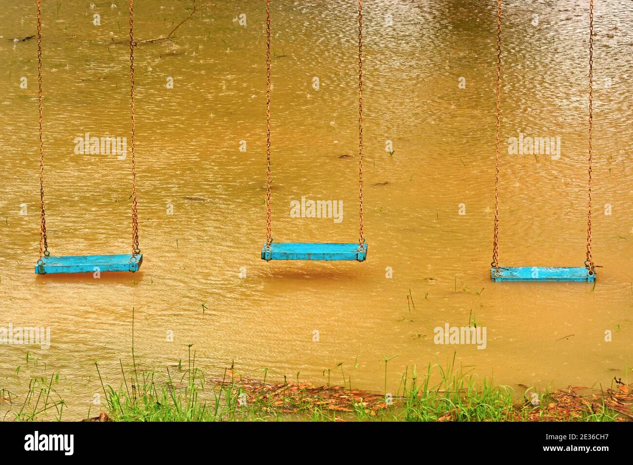 Playground swings with flooded ground and grass underneath Stock Photo