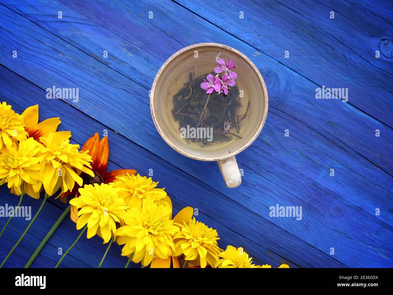 Natural herbal tea with purple fresh flowers and leaves of medical fireweed plant n ceramic cup on blue wooden boards outdoors. Stock Photo