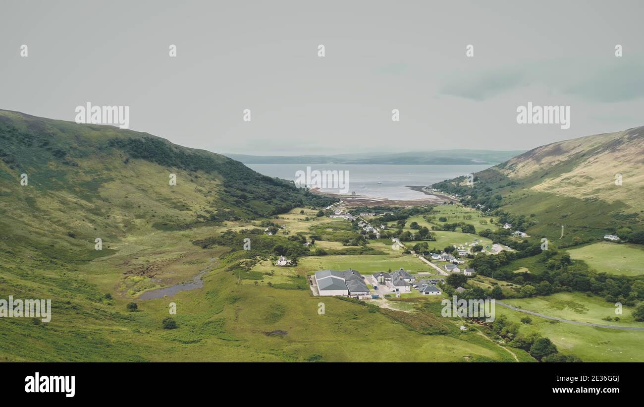 Village at green mountain valley aerial. Scottish hillside town with sea lake, castle ruins. Rural nobody nature landscape. Whiskey distillery at Lochranza countryside, Arran Island, Scotland, Europe Stock Photo