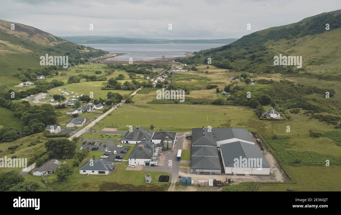 Green mountain valley village aerial. Scottish nature landscape of hillside town with sea lake, castle ruin. Countryside whisky distillery at Loch-Ranza, Arran Island, Scotland, Europe. Cinematic shot Stock Photo